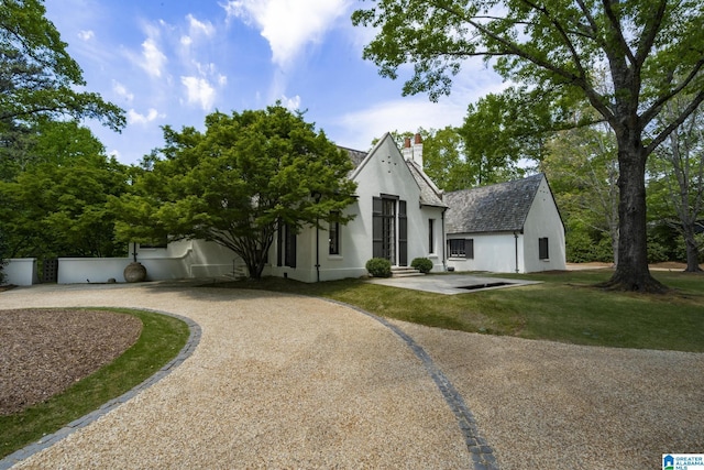 view of front of house featuring curved driveway, a chimney, stucco siding, and a front lawn