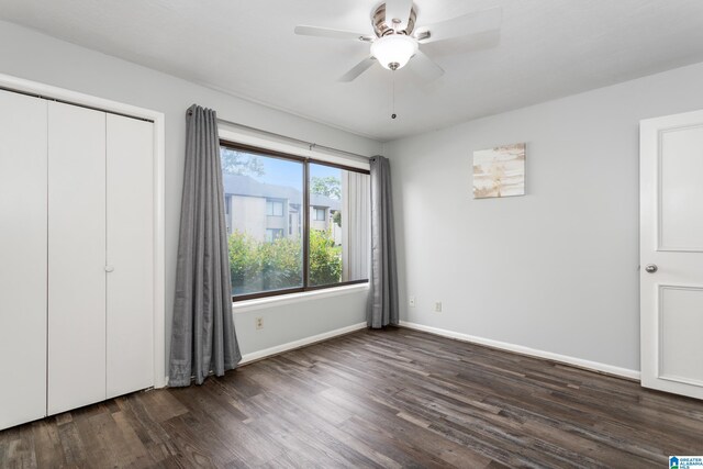unfurnished bedroom with dark wood-style floors, baseboards, a ceiling fan, and a closet