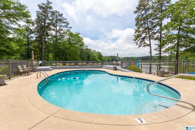 community pool featuring fence, a patio, and view of wooded area