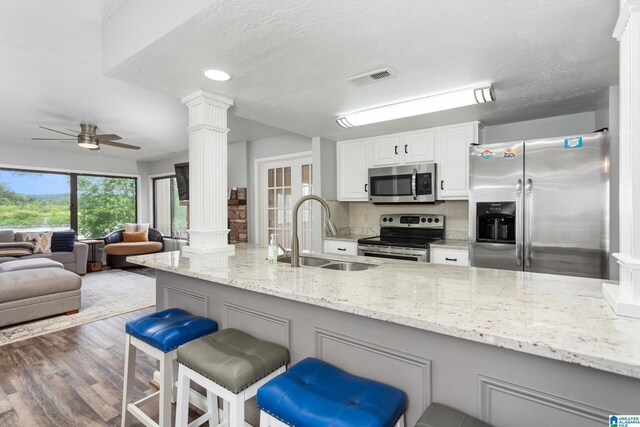 kitchen featuring stainless steel appliances, a sink, decorative columns, ceiling fan, and a kitchen breakfast bar