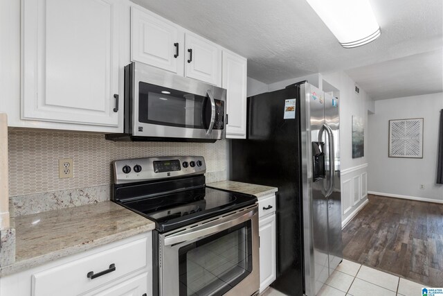 kitchen featuring appliances with stainless steel finishes, white cabinetry, tasteful backsplash, light tile patterned flooring, and light stone countertops