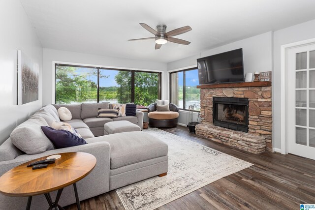 living area featuring a ceiling fan, a stone fireplace, and wood finished floors