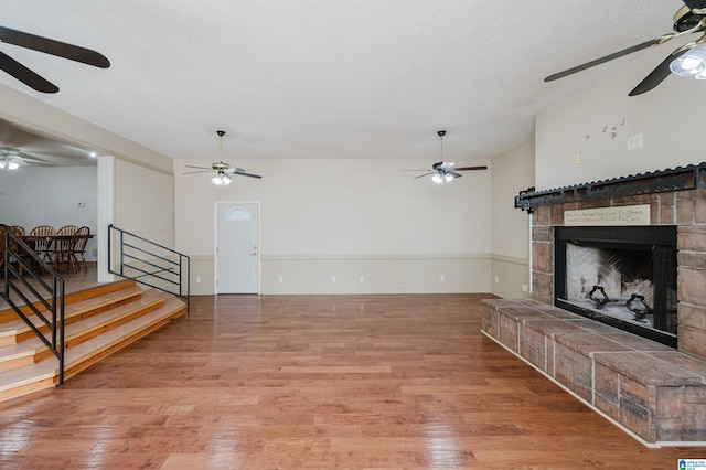 1492 Paul Allman Rd, Adger, AL 35006 - unfurnished living room with a ceiling fan, wood finished floors, a fireplace with raised hearth, stairway, and a textured ceiling