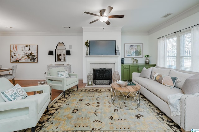 living room with crown molding, a ceiling fan, wood finished floors, a fireplace, and baseboards