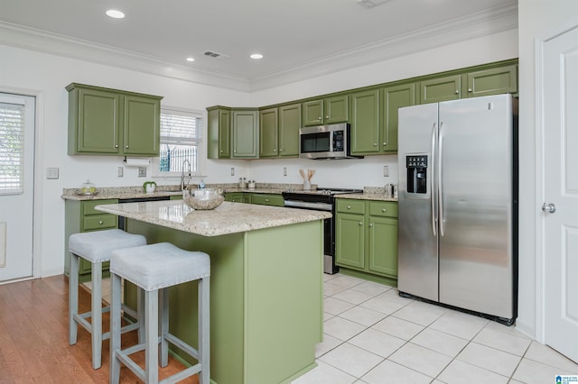 kitchen with green cabinetry, appliances with stainless steel finishes, a breakfast bar, a kitchen island, and crown molding