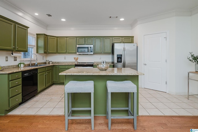 kitchen with green cabinetry, stainless steel appliances, a sink, crown molding, and a kitchen bar