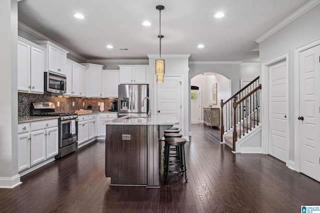 kitchen featuring appliances with stainless steel finishes, arched walkways, a sink, tasteful backsplash, and light stone countertops
