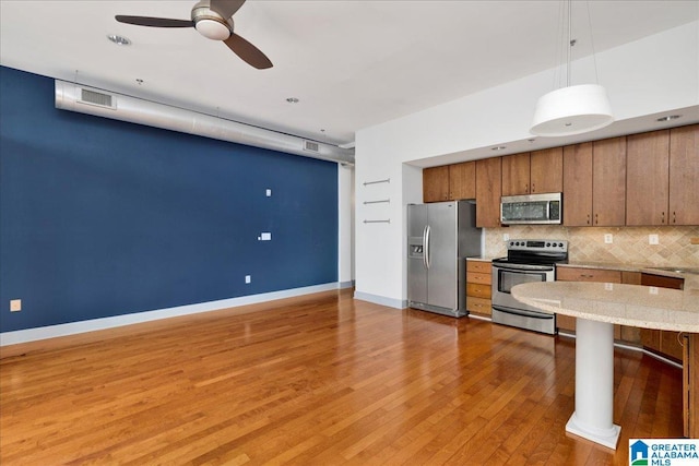 kitchen with appliances with stainless steel finishes, brown cabinets, hanging light fixtures, tasteful backsplash, and light wood finished floors