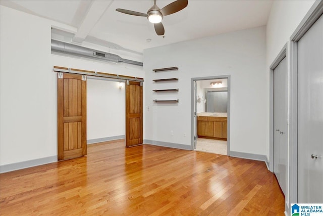 unfurnished bedroom featuring light wood-type flooring, ensuite bathroom, baseboards, and beam ceiling