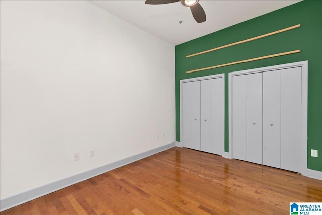 unfurnished bedroom with two closets, wood finished floors, baseboards, and a ceiling fan