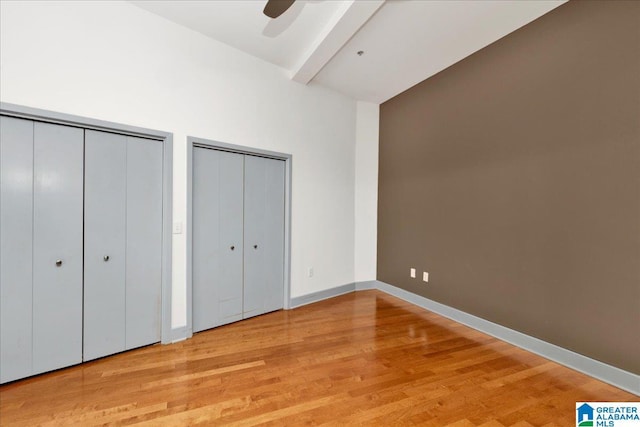 unfurnished bedroom with two closets, beamed ceiling, wood finished floors, a ceiling fan, and high vaulted ceiling