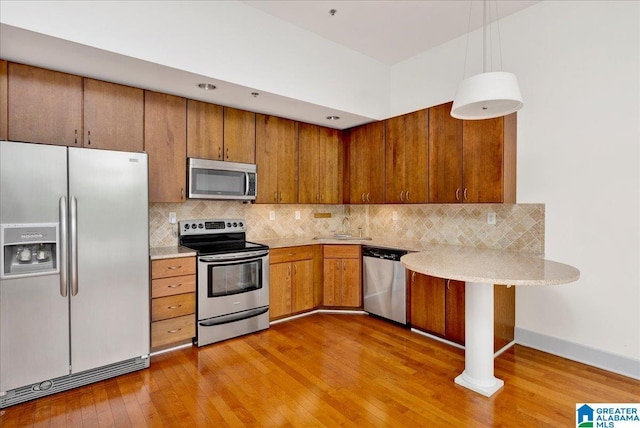 kitchen with appliances with stainless steel finishes, brown cabinetry, a sink, light wood-type flooring, and backsplash