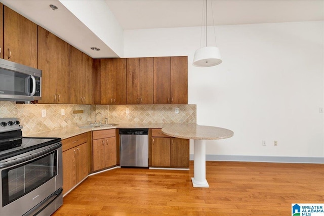 kitchen with appliances with stainless steel finishes, a sink, brown cabinets, decorative backsplash, and light wood-style flooring