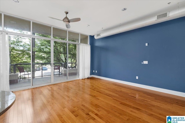 unfurnished room with ceiling fan, wood-type flooring, plenty of natural light, a wall of windows, and baseboards