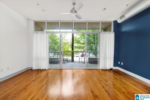 spare room featuring floor to ceiling windows, ceiling fan, wood-type flooring, and baseboards