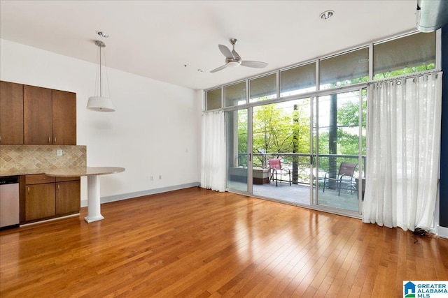 unfurnished living room featuring ceiling fan, a wall of windows, light wood finished floors, and baseboards