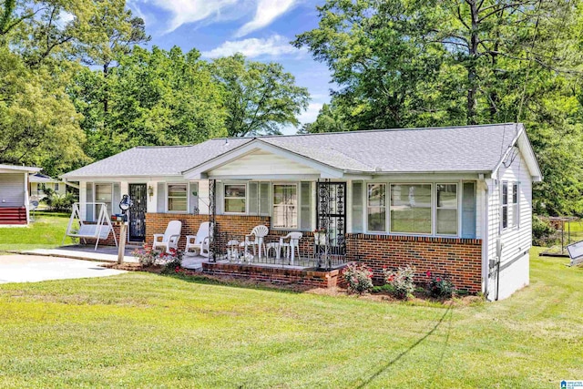 bungalow featuring covered porch, a front yard, brick siding, and a shingled roof