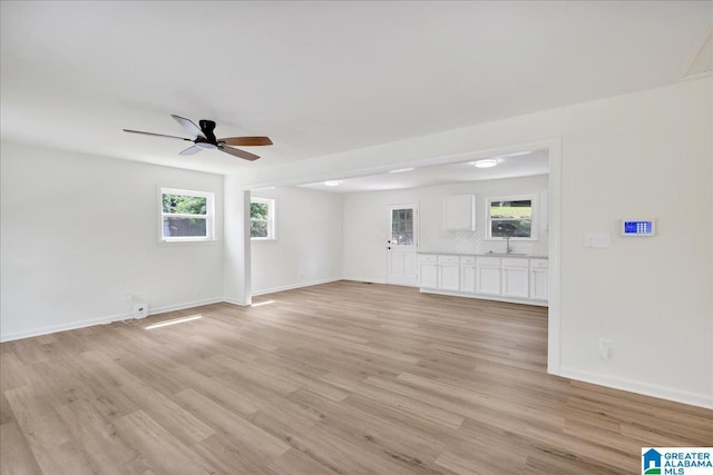 unfurnished living room with a ceiling fan, light wood-style flooring, plenty of natural light, and baseboards