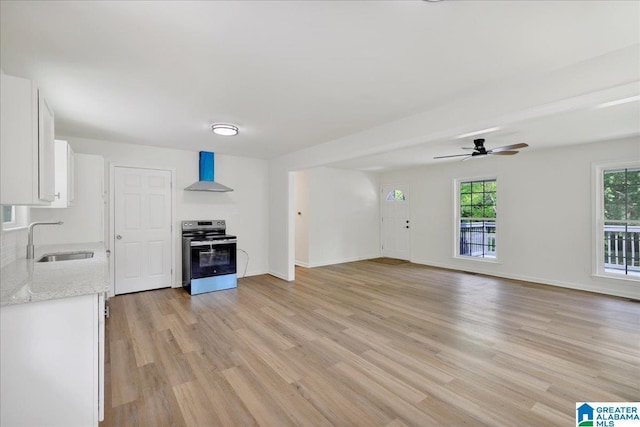 unfurnished living room with a sink, light wood-type flooring, a ceiling fan, and baseboards