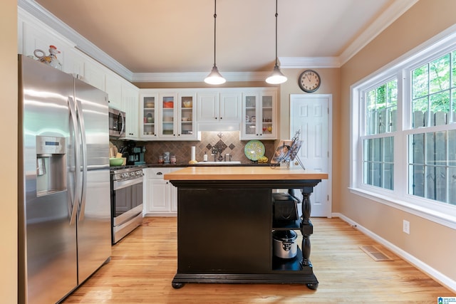 kitchen with stainless steel appliances, crown molding, decorative backsplash, white cabinetry, and hanging light fixtures