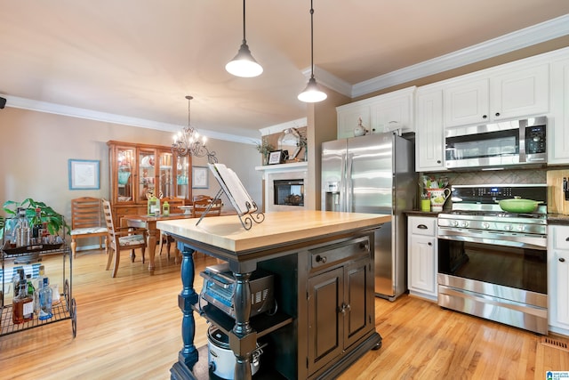 kitchen with appliances with stainless steel finishes, butcher block countertops, white cabinetry, ornamental molding, and backsplash