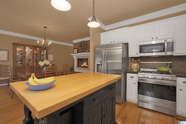 kitchen featuring appliances with stainless steel finishes, white cabinets, crown molding, backsplash, and pendant lighting