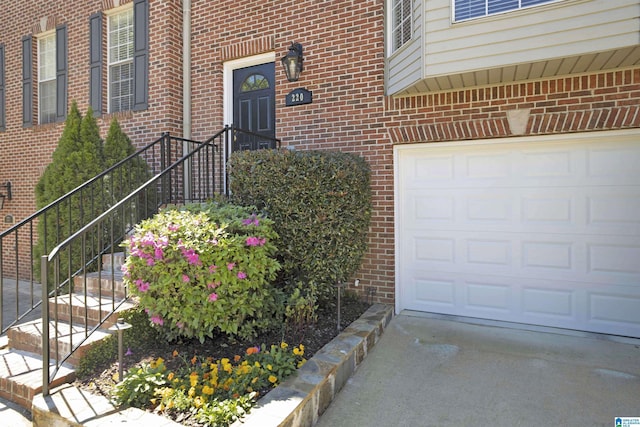 view of exterior entry featuring brick siding, a garage, and driveway