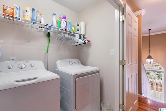 clothes washing area with washing machine and dryer, wood finished floors, baseboards, and crown molding