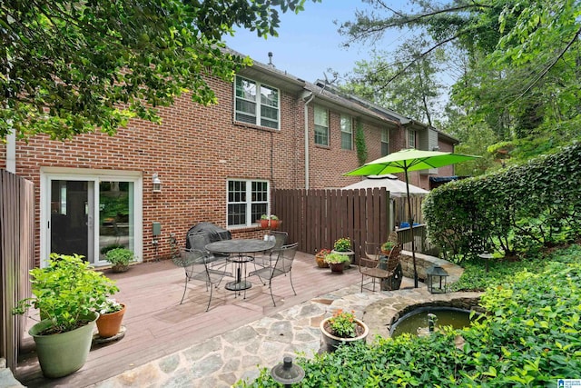 back of property with a wooden deck, brick siding, outdoor dining space, and fence