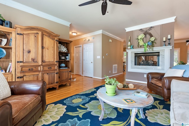 living area with crown molding, ceiling fan, light wood-style floors, a multi sided fireplace, and baseboards