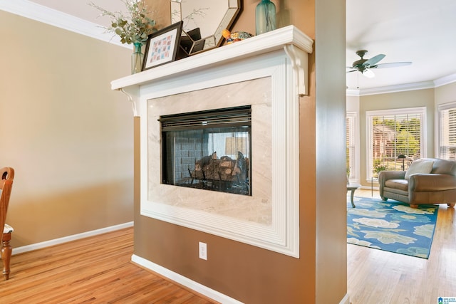 detailed view of ornamental molding, wood finished floors, baseboards, a ceiling fan, and a fireplace