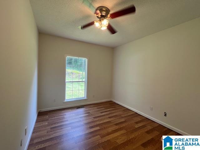 empty room with ceiling fan, wood finished floors, baseboards, and a textured ceiling