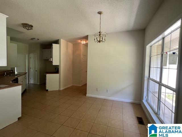 unfurnished dining area with a textured ceiling, a chandelier, light tile patterned floors, baseboards, and a sink