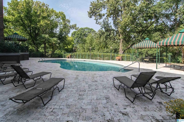 view of swimming pool featuring fence, a patio area, and view of scattered trees