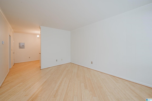 empty room featuring wood finished floors, electric panel, ornamental molding, and baseboards