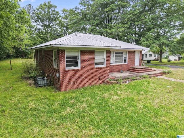 view of side of home with central AC unit, a yard, crawl space, metal roof, and brick siding
