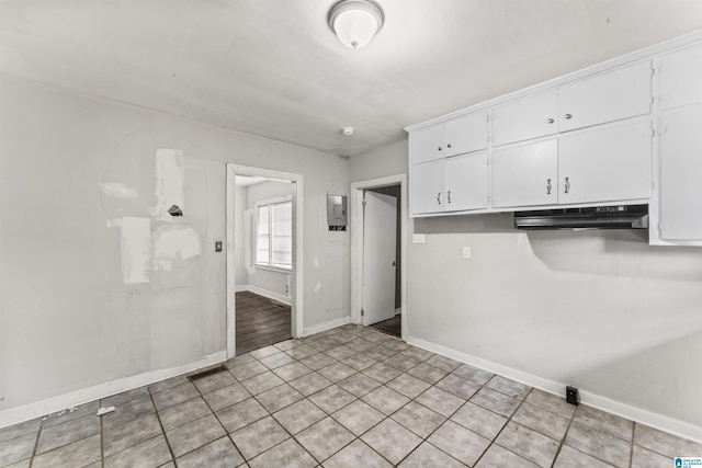 kitchen with under cabinet range hood, white cabinetry, baseboards, electric panel, and light tile patterned flooring
