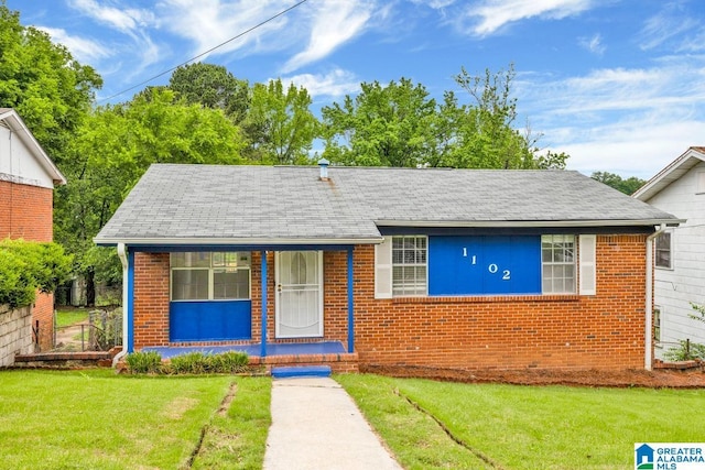 bungalow with a front yard, brick siding, and roof with shingles