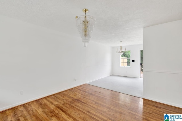 unfurnished room with a chandelier, wood finished floors, and baseboards