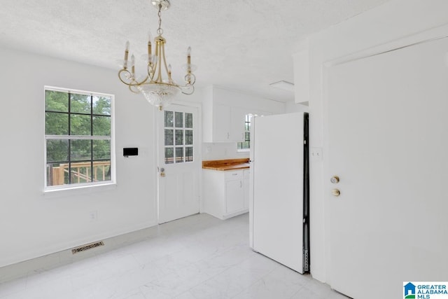 unfurnished dining area featuring a chandelier, light marble finish flooring, and a textured ceiling