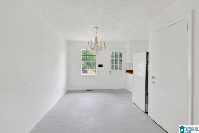 spare room with a chandelier, light marble finish floors, a textured ceiling, and baseboards