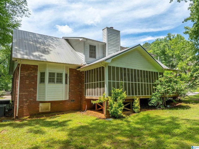 back of property with a chimney, a sunroom, brick siding, a yard, and central air condition unit