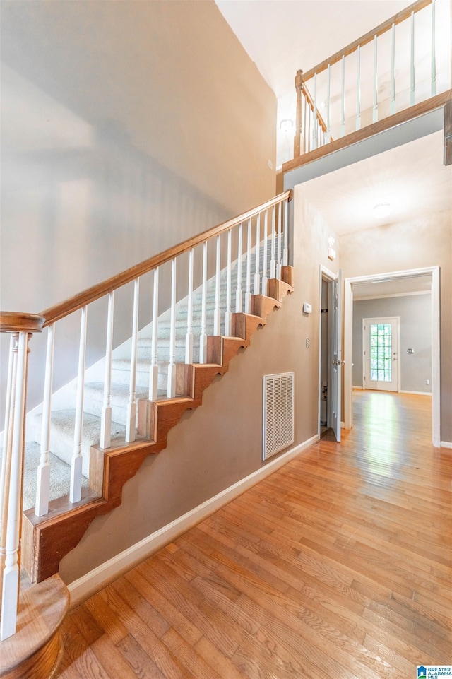staircase featuring wood finished floors, a towering ceiling, and baseboards