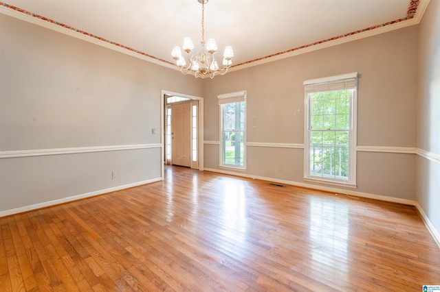unfurnished room with a chandelier, light wood finished floors, baseboards, and ornamental molding