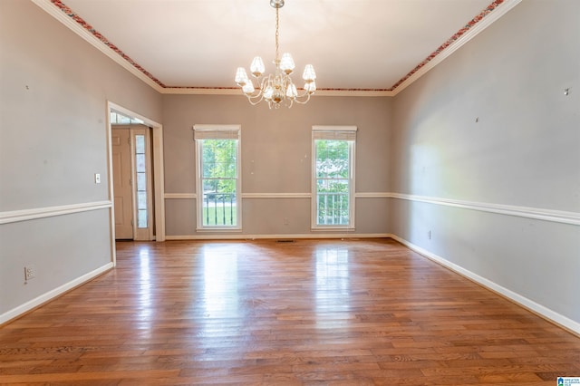 spare room featuring a chandelier, ornamental molding, wood finished floors, and baseboards