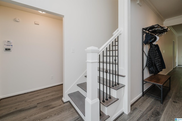 staircase with wood finished floors, ornamental molding, and baseboards