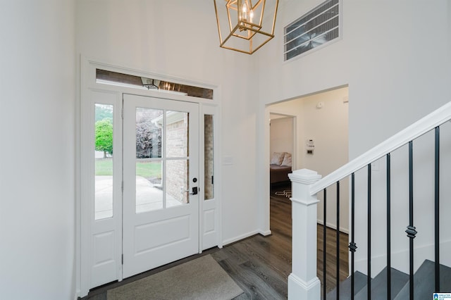 foyer entrance with dark wood-style floors, stairs, a chandelier, and a towering ceiling