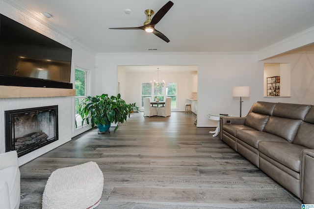 living room with a chandelier, ceiling fan, crown molding, wood finished floors, and healthy amount of natural light