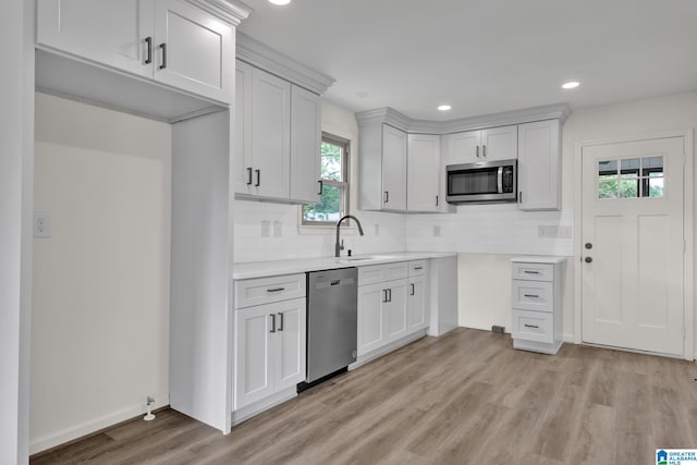 kitchen featuring appliances with stainless steel finishes, a sink, light wood finished floors, tasteful backsplash, and recessed lighting