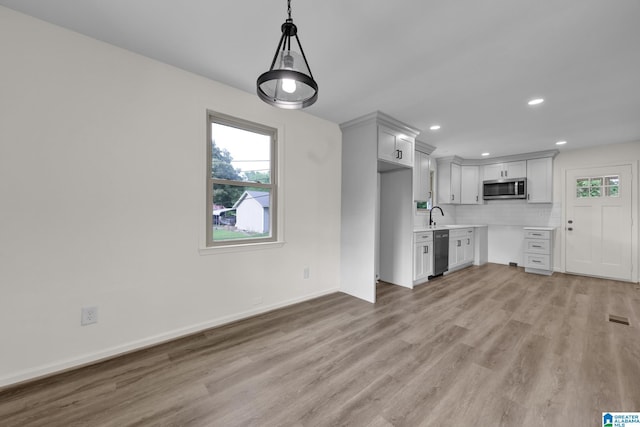 kitchen with stainless steel microwave, dishwashing machine, light wood finished floors, light countertops, and recessed lighting